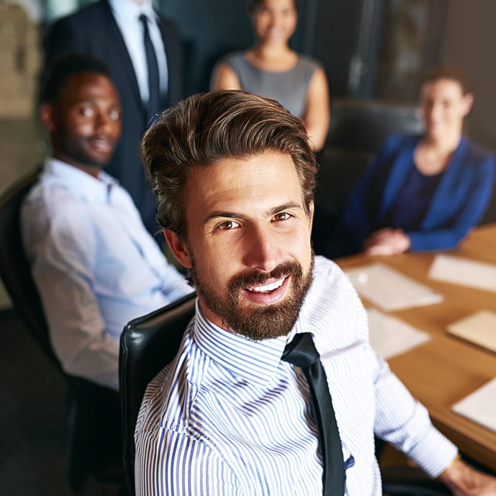 Portrait of a smiling businessman sitting in an office with colleagues in the background