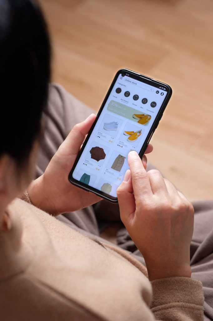 close up hand browsing shopping fashion mobile app on sofa at home