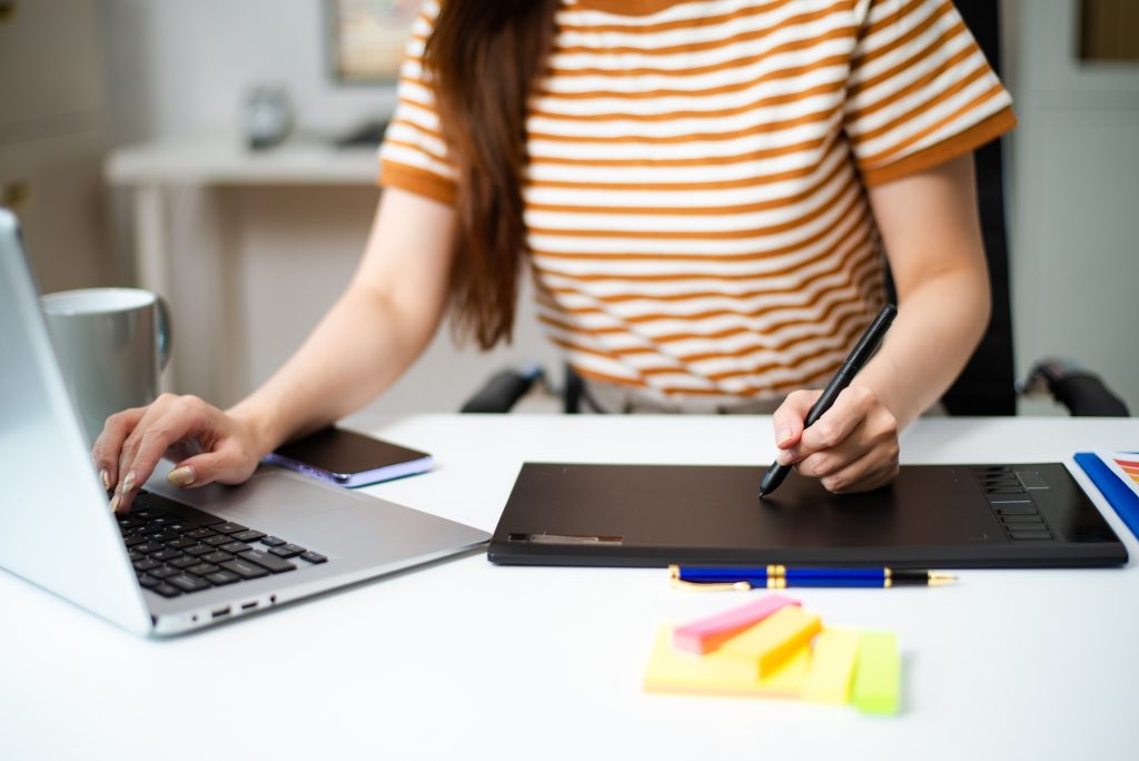 Creative woman working on digital tablet and laptop at desk. Ideal for themes like freelance design,