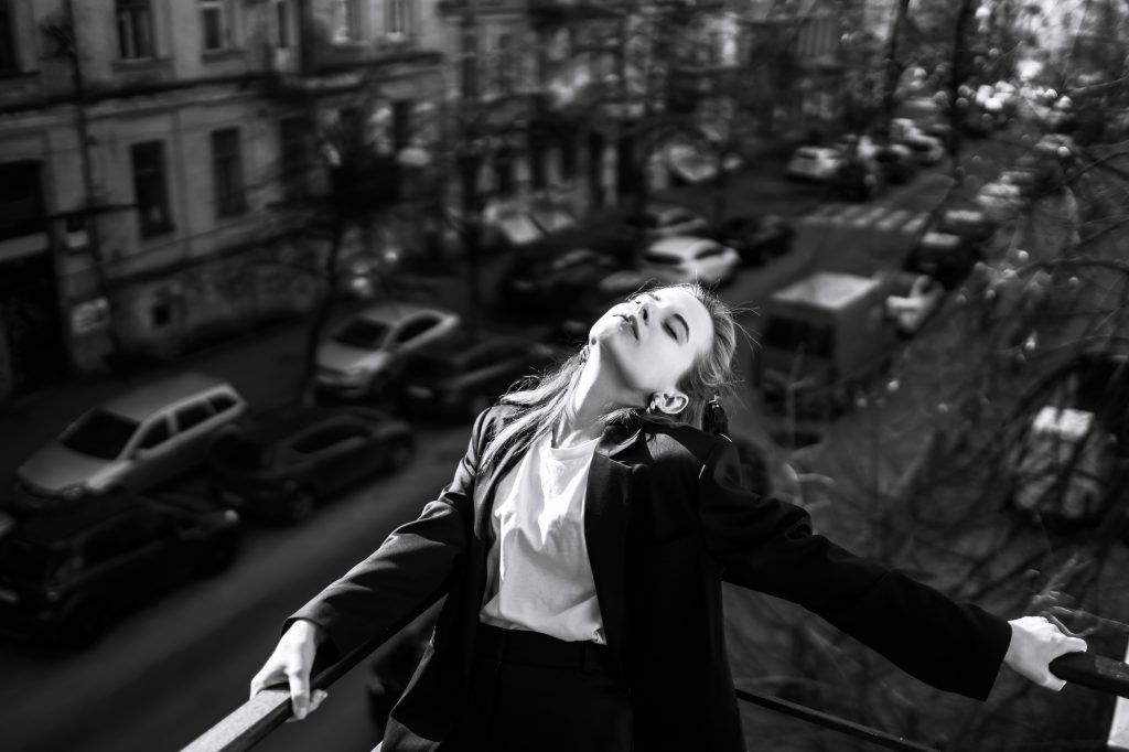 Black and white photo of stylish woman posing on balcony in city. Spring autumn fashion concept.