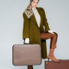 full length of trendy woman in green coat and headscarf posing with retro suitcases on grey